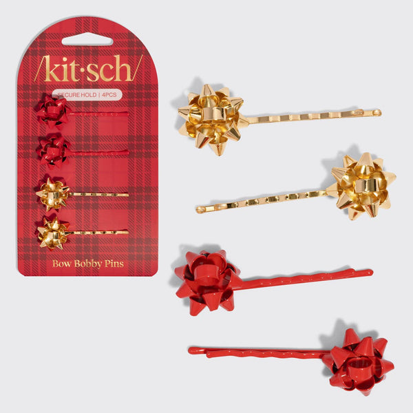 A set of six bow-shaped bobby pins in red and gold, shown with their retail packaging on a light gray background. The packaging is red plaid with gold lettering that reads 'kit:sch' and 'GIFT HOLE PINS'.